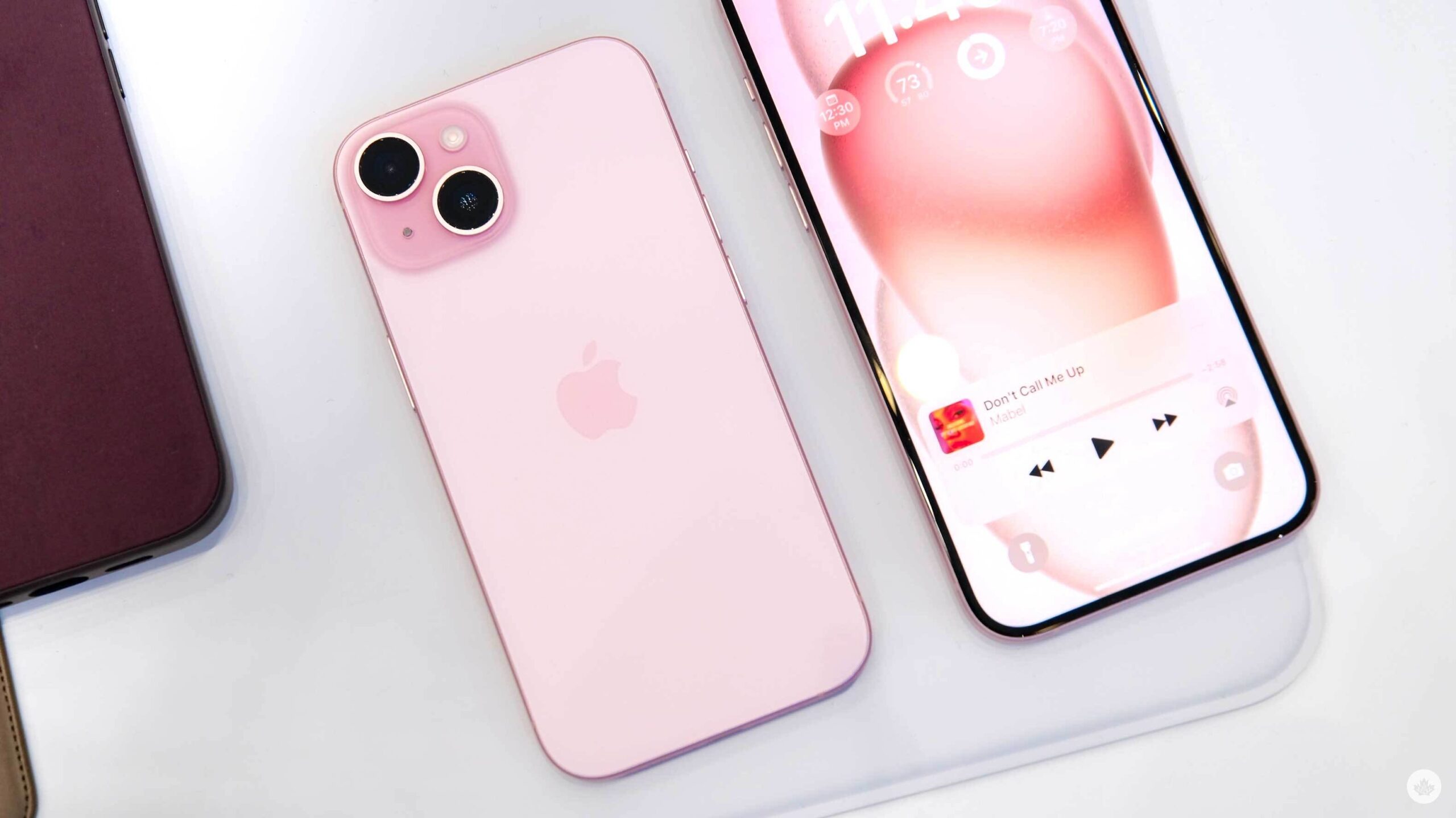 Dos teléfonos táctiles iPhone 15 color rosa sobre una superficie blanca, uno de espalda y otro de frente