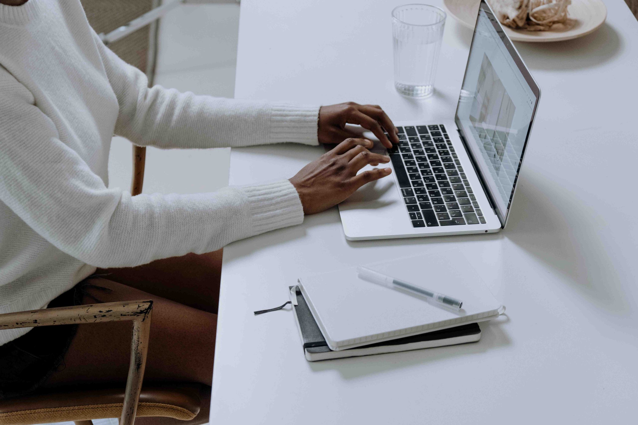 Mujer de camisa blanca usando una laptop negra de teclas negras en una mesa blanca con libretas de nota