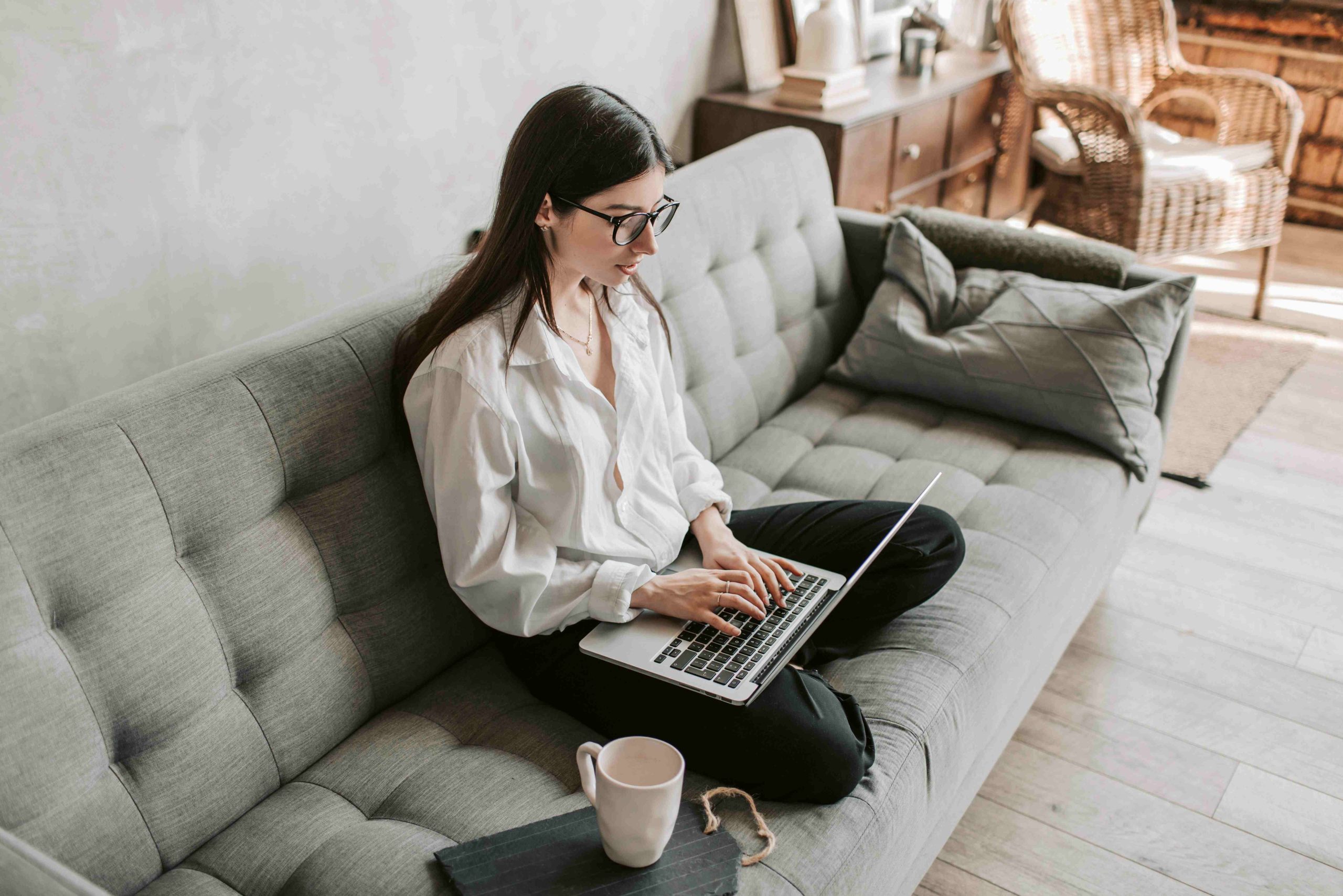 Chica sentada en un sofá gris usando una laptop plateada de teclas negras